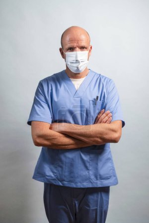 Photo for Portrait of a physiotherapist in light blue gown and face mask looking at camera in studio. - Royalty Free Image