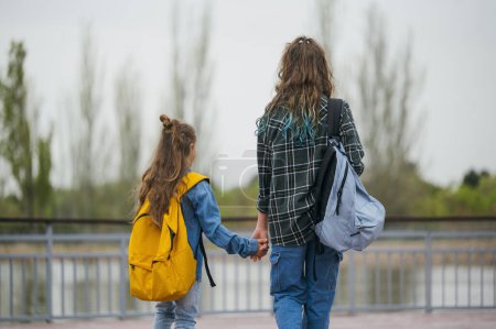 Téléchargez les photos : Une adolescente qui va à l'école avec son petit frère. - en image libre de droit