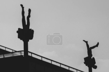 Photo for The silhouette with sculptures of upside-down people creates a retro vibe. Two sculptures on the background of the sky at sunset. - Royalty Free Image