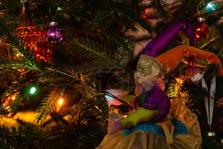 Foto de Un arlequín de juguete como decoración de Año Nuevo en el fondo de un árbol de Navidad festivamente decorado con juguetes y linternas. Ambiente festivo de Año Nuevo. - Imagen libre de derechos