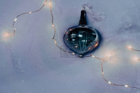 Foto de El juguete azul oscuro del árbol de Navidad miente en la nieve brillante blanca rodeada por una guirnalda con la luz caliente de las linternas en la luz de la tarde, vista de arriba. Fondo de invierno con nieve con decoración festiva brillante. - Imagen libre de derechos