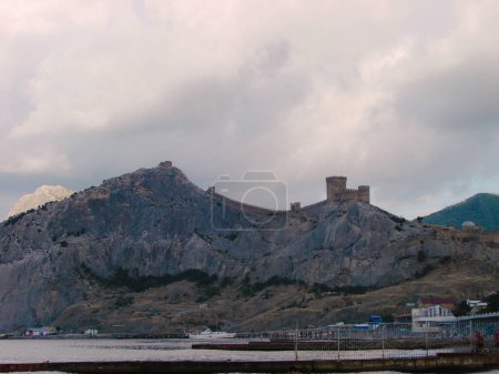 An ancient medieval fortress on the edge of a cliff is surrounded by storm clouds. Landscape of a tourist and historical place.