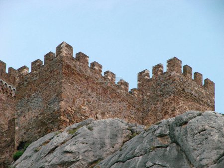 A fortress in the Romanesque style of the time of the knights, which stands on the edge of a stone cliff. Architectural building of the Middle Ages against the background of rocky nature.