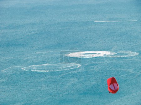 Top view of white circles on sea water above which a red cap flies.