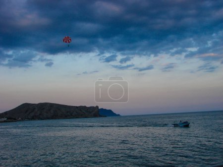 Foto de Kitesurfer en el cielo al atardecer sobre el fondo del mar y el cielo. Un barco a motor está navegando en el agua de mar a alta velocidad. - Imagen libre de derechos