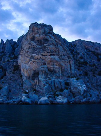 Foto de Una roca con una textura distinta del suelo se encuentra por encima del agua tranquila. Pintoresco paisaje de montaña al atardecer con un agradable tinte azul. - Imagen libre de derechos