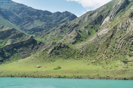 Foto de Kyrgyzstan green landscape with a yurt tent beside vast mountains. Kyrgyzstan is a landlocked country located in central Asia, known for its rugged, mountainous terrain and verdant grasslands. - Imagen libre de derechos