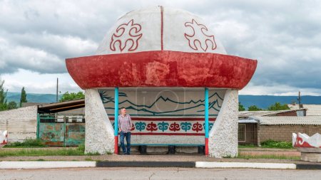 Photo for Kyrgyzstan - May 2022: Man waiting at the Kyrgyz bus stop, which is in the shape of traditional central asian kalpak hat. - Royalty Free Image