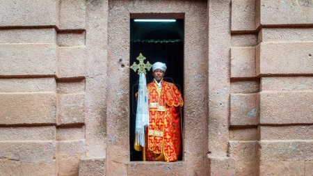 Téléchargez les photos : Lalibela, Éthiopie - 24 octobre 2023 : Un prêtre tenant une croix chrétienne à l'entrée d'une église taillée dans un rocher à Lalibela, sculptée dans un rocher massif - en image libre de droit