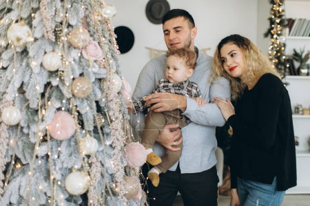 Téléchargez les photos : Portrait de famille heureuse de père mère et petit fils bouclé célébrant Noël ensemble à la maison. Le concept du réveillon du Nouvel An. - en image libre de droit