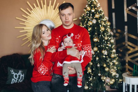 Photo for Happy family mom dad and little daughter in red traditional Christmas clothes spending time together near Christmas tree, copy space - Royalty Free Image