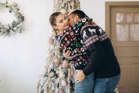 Foto de Pareja feliz en jersey tradicional decorando el árbol de Navidad juntos en casa - Imagen libre de derechos