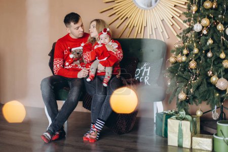 Foto de Feliz familia mamá papá y su hija pequeña en rojo ropa de Navidad tradicional pasar tiempo juntos cerca del árbol de Navidad, espacio para copiar - Imagen libre de derechos