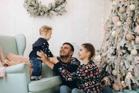 Téléchargez les photos : Portrait de famille heureuse de père mère et petit fils bouclé célébrant Noël ensemble à la maison. Le concept du réveillon du Nouvel An. - en image libre de droit