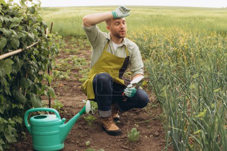 Téléchargez les photos : Un agriculteur masculin travaille dans le jardin et montre de la fatigue - en image libre de droit