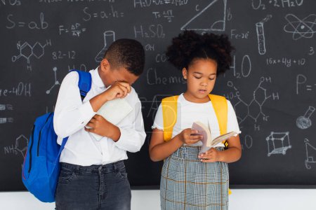 Téléchargez les photos : Écolière afro-américaine et écolier métis résolvant des problèmes près de la commission scolaire, concept de retour à l'école. - en image libre de droit