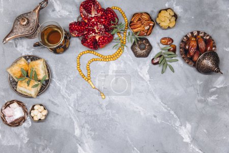 Foto de Elegante pancarta con vajilla árabe tradicional y juegos de alimentos, taza de té, Corán y rosario sobre fondo de piedra gris. Vista superior de la mesa de Ramadán - Imagen libre de derechos