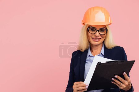 Photo for Portrait of attractive mature business woman architect or engineer in glasses use folder with documents on the pink background - Royalty Free Image