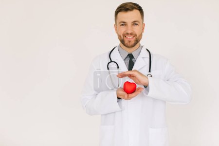 Foto de El médico cardiólogo varón feliz sosteniendo el corazón sobre fondo blanco - Imagen libre de derechos