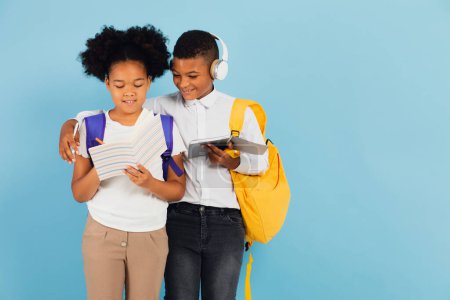 Photo for African schoolboy and African American schoolgirl are reading outline together in school classroom on blue background, back to school concept. - Royalty Free Image