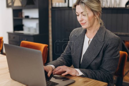 Téléchargez les photos : Femme d'affaires mature administrateur de restaurant assis et travaillant sur ordinateur portable - en image libre de droit