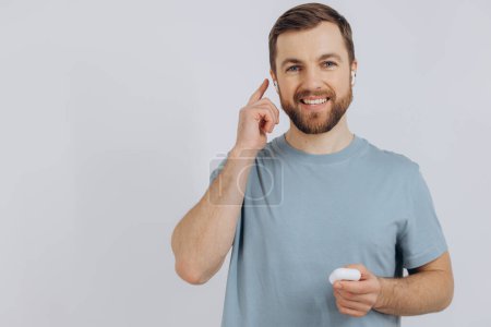 Photo for Portrait of modern millennial man with beard holding wireless earphones on white background with copy space - Royalty Free Image