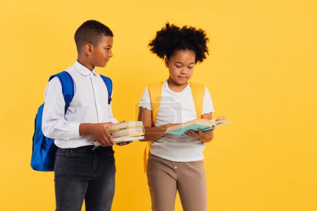 Foto de Feliz colegiala afroamericana y colegial de raza mixta sosteniendo libros sobre fondo amarillo, espacio para copiar. - Imagen libre de derechos