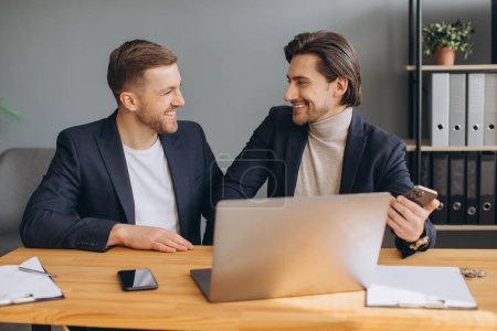 Téléchargez les photos : Travail d'équipe - deux hommes d'affaires souriants qui travaillent ensemble sur un ordinateur portable - en image libre de droit