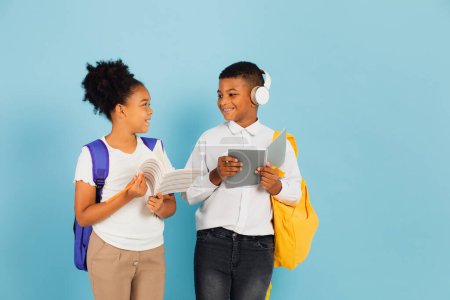 Téléchargez les photos : Un écolier africain et une écolière afro-américaine lisent ensemble dans une salle de classe sur fond bleu, concept de retour à l'école. - en image libre de droit
