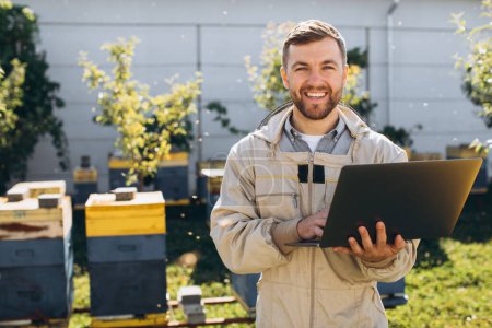 Foto de Hombre agrónomo o ingeniero en traje de protección que trabaja en el ordenador portátil en la granja de abejas - Imagen libre de derechos