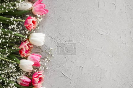 Photo for Pink tulips and white gypsophila flowers bouquet on a stylish gray stone background. Mothers Day, birthday celebration concept. Copy space for text - Royalty Free Image
