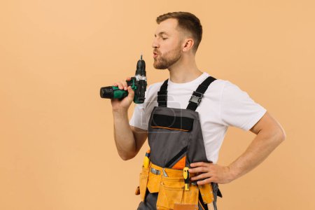 Foto de Reparador masculino positivo en casa con destornillador sobre fondo beige - Imagen libre de derechos