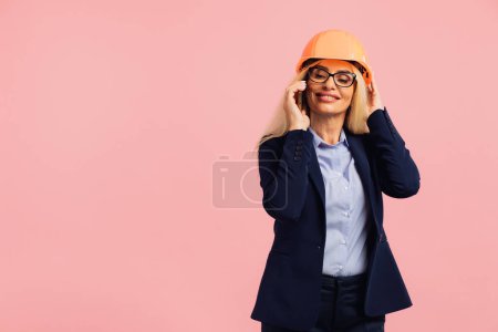Foto de Arquitecta mujer en gafas utilizar la llamada de teléfono móvil con ingeniero o gerente de proyecto en el fondo rosa - Imagen libre de derechos
