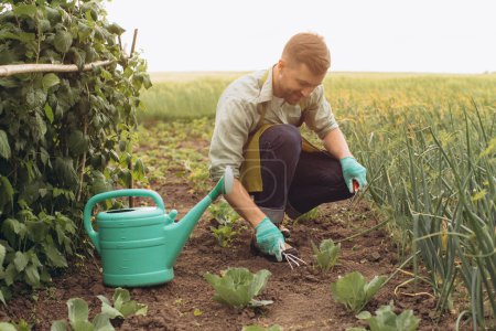 Téléchargez les photos : Homme fermier heureux arrose les lits et travaille dans le jardin - en image libre de droit