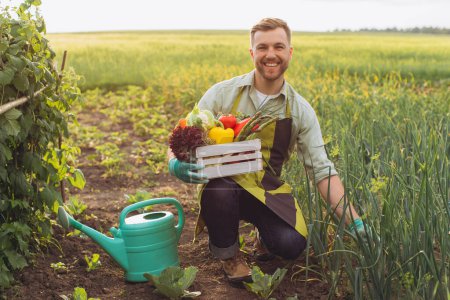 Foto de Hombre agricultor feliz sosteniendo cesta con verduras frescas y trabajando en el jardín, concepto de jardinería - Imagen libre de derechos