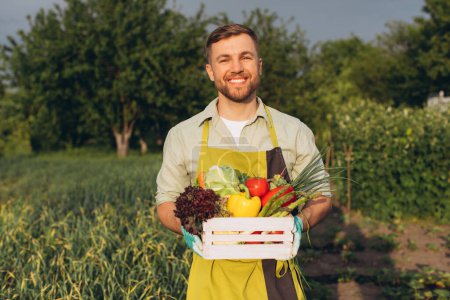 Photo for Happy farmer man holding basket with fresh vegetables on rainbow and garden background, gardening concept - Royalty Free Image