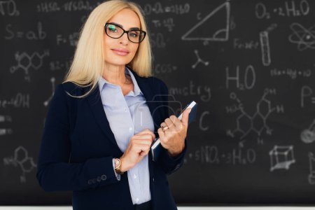 Téléchargez les photos : Portrait d'une enseignante blonde heureuse debout près du tableau noir dans la salle de classe. - en image libre de droit