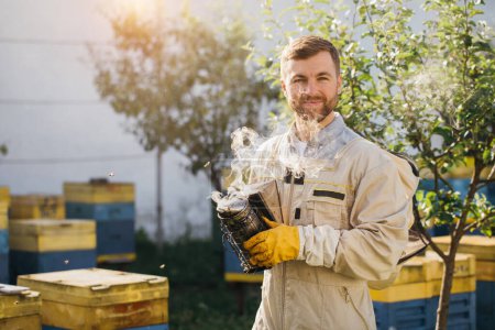 Photo for Portrait of the male beekeeper smoking the honeycomb of a beehive with bees swarming around them - Royalty Free Image