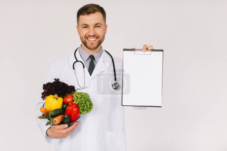 Foto de El médico nutricionista masculino con estetoscopio sosteniendo verduras frescas y carpeta con espacio de copia con sobre fondo blanco - Imagen libre de derechos