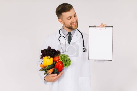 Photo for The male doctor nutritionist with stethoscope holding fresh vegetables and folder with copy space with on white background - Royalty Free Image