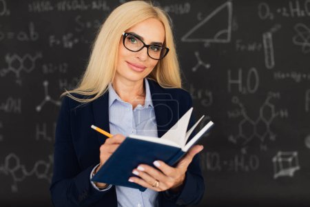 Photo for Portrait of happy blonde teacher woman standing near the blackboard in the classroom. - Royalty Free Image
