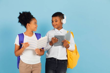 Photo for African schoolboy and African American schoolgirl are reading outline together in school classroom on blue background, back to school concept. - Royalty Free Image