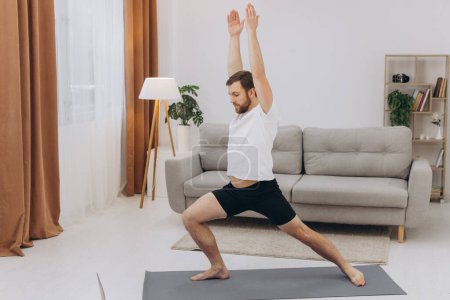 Photo for Positive athletic bearded middle-aged man stretching at home, using laptop, watching sport videos on Internet, having fitness class online, copy space. Healthy lifestyle, sport on self-isolation - Royalty Free Image