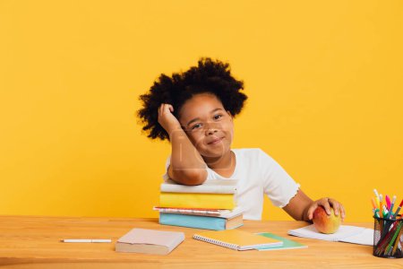 Foto de Feliz colegiala afroamericana haciendo la tarea mientras está sentada en el escritorio. Regreso al concepto escolar. - Imagen libre de derechos