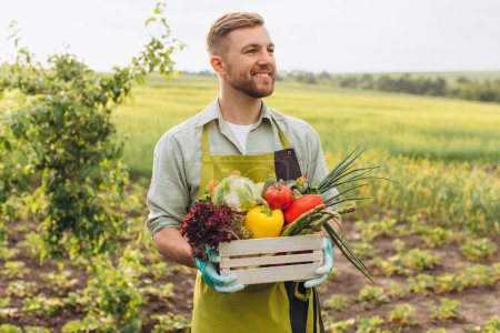 Téléchargez les photos : Heureux agriculteur homme panier d'exploitation avec légumes frais dans le jardin, concept de jardinage - en image libre de droit