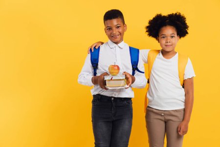 Photo for Happy african american schoolgirl and mixed race schoolboy holding books side by side on yellow background. Back to school concept. - Royalty Free Image