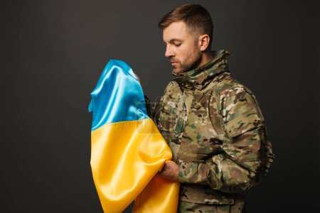Portrait of a courageous Ukrainian military man holding the flag of Ukraine, freedom concept