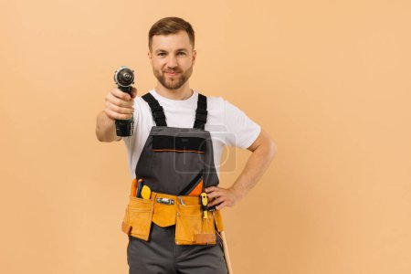 Foto de Reparador masculino positivo en casa con destornillador sobre fondo beige - Imagen libre de derechos