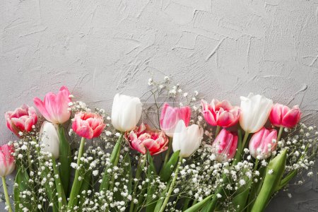 Photo for Pink tulips and white gypsophila flowers bouquet on a stylish gray stone background. Mothers Day, birthday celebration concept. Copy space for text - Royalty Free Image