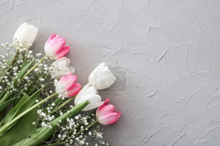 Photo for Pink tulips and white gypsophila flowers bouquet on a stylish gray stone background. Mothers Day, birthday celebration concept. Copy space for text. Mockup - Royalty Free Image